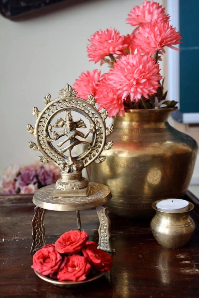 table set up with brass vessels, pooja stand, statue and flowers, a vintage decor arrangement