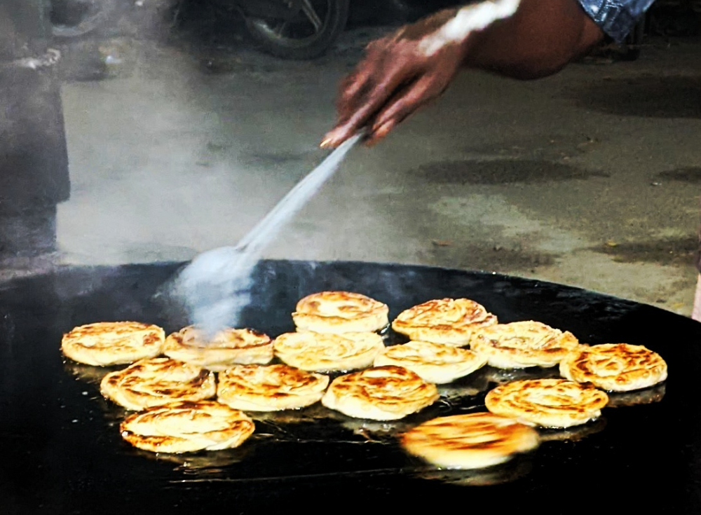 seller tossing around bun parotta on a hot tawa