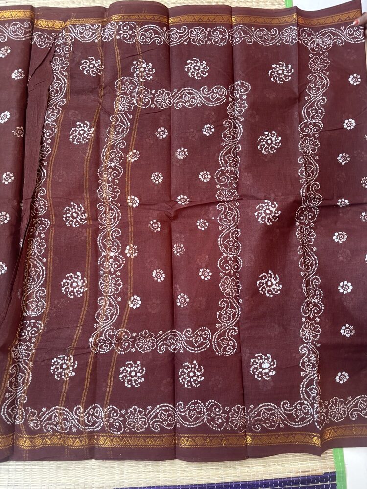 Brown sungudi batik saree with white floral rosette motifs, gold zari border and framed floral pallu with wave accents