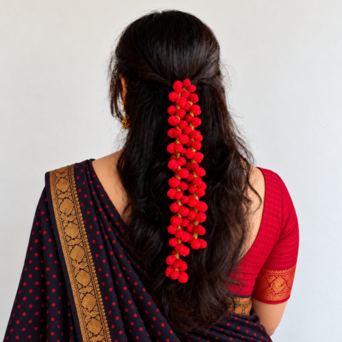 Artificial red rose bud string crocheted from woollen yarn, worn in a half-up hairstyle with a saree