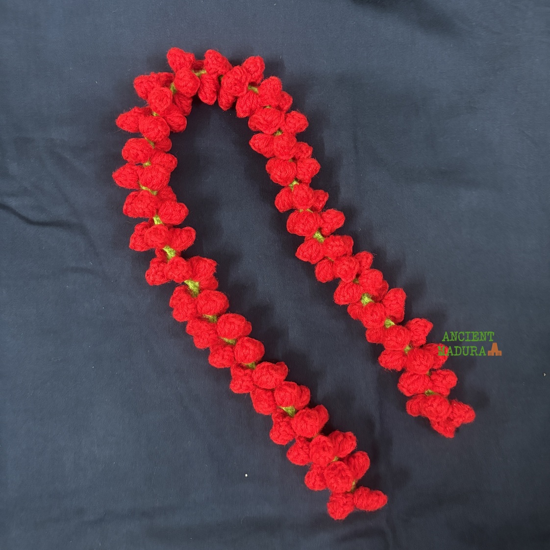 Artificial red rose bud string crocheted from woollen yarn, worn in a half-up hairstyle with a saree